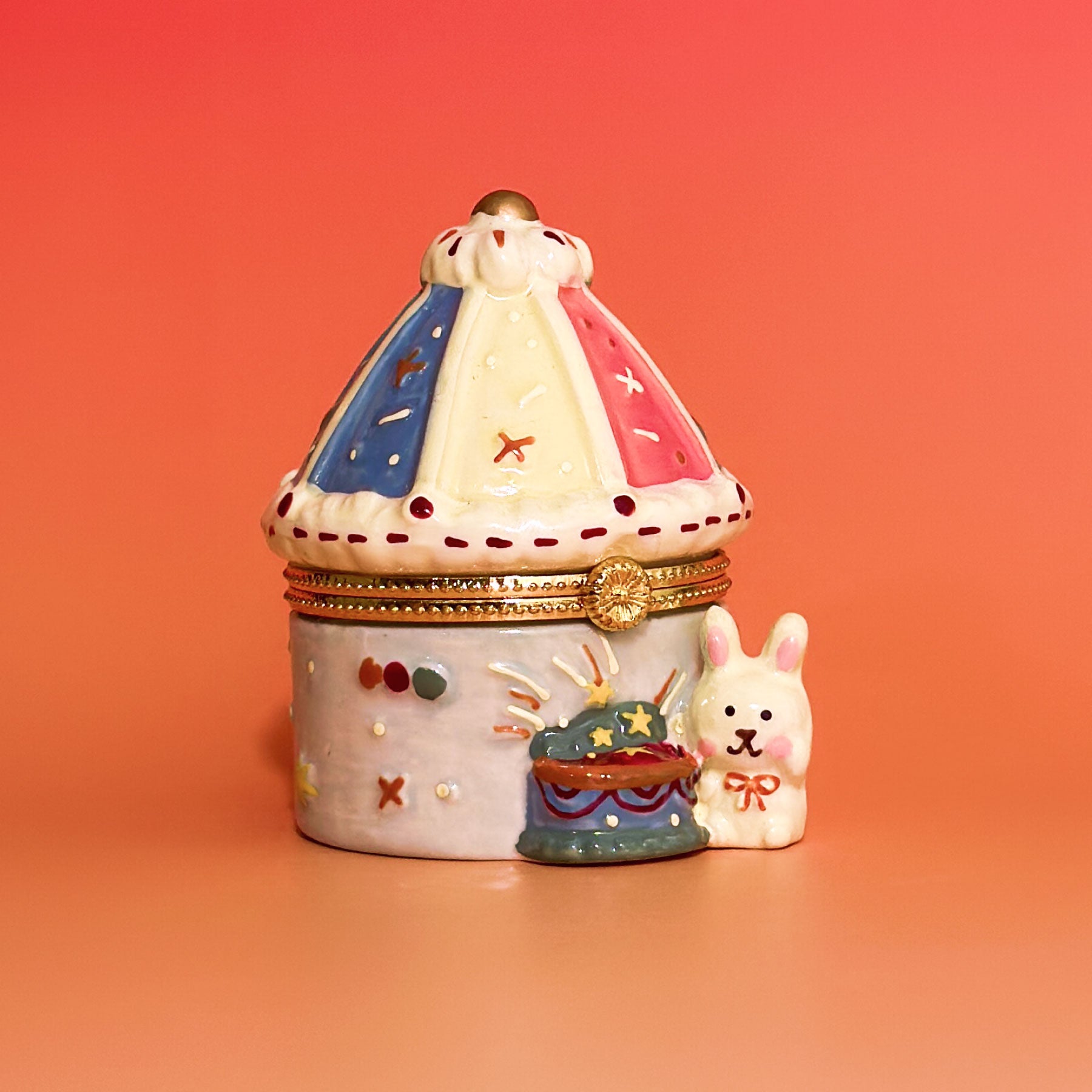 Front view of hand-painted carousel trinket box with pastel tent roof and ceramic bunny figurine.