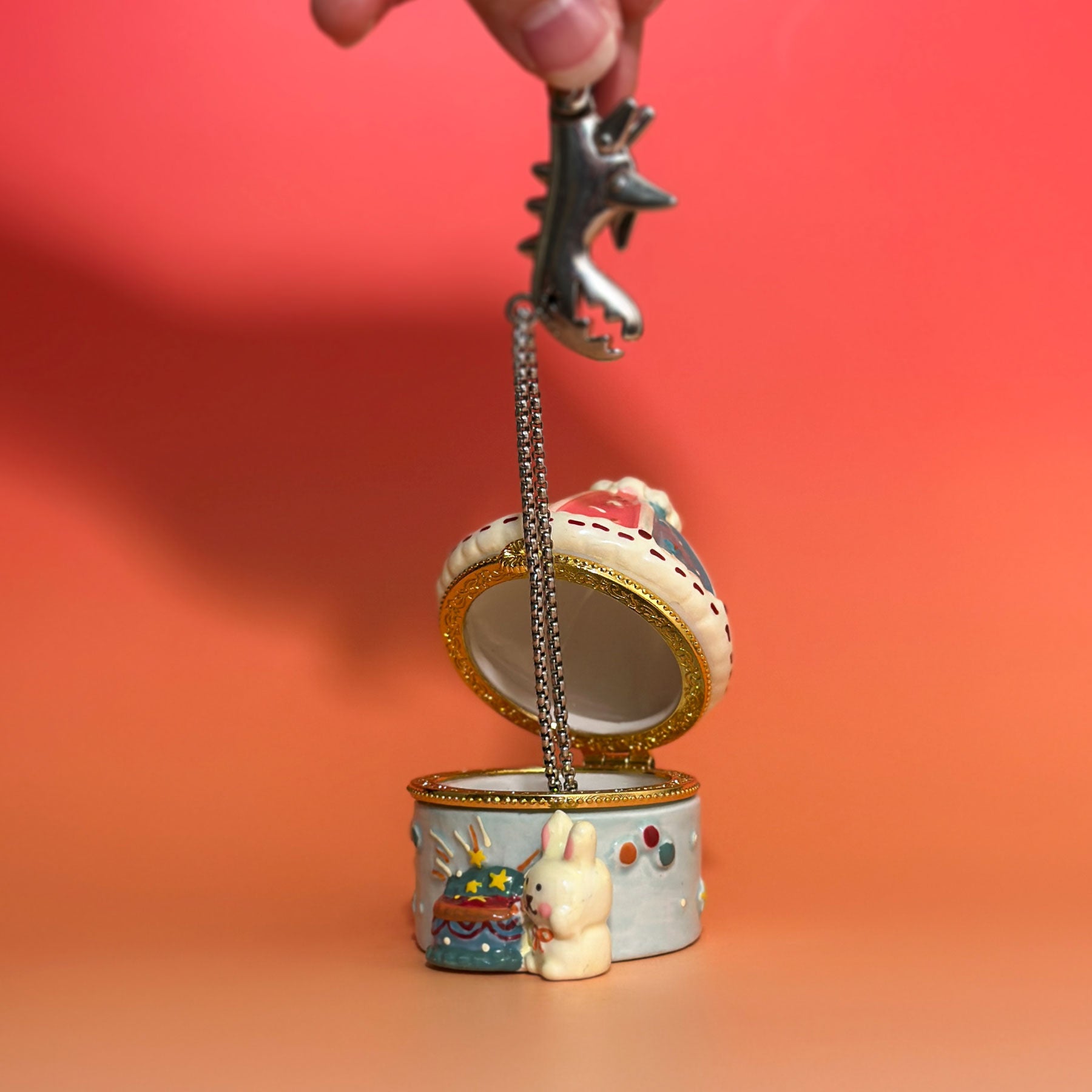 Open carousel bunny trinket box holding jewelry, showing interior compartment and gold metal hinge.