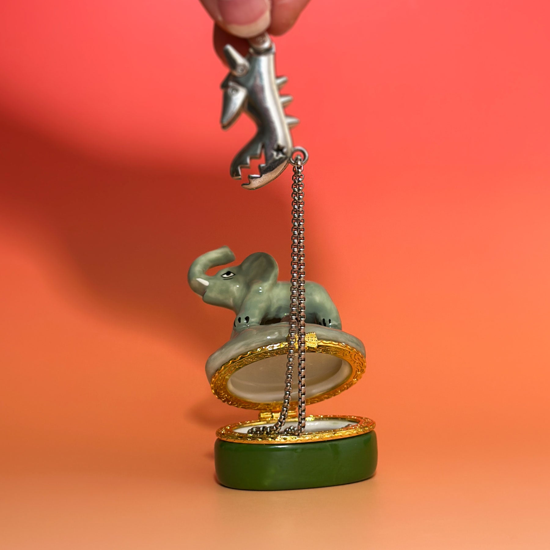 Open elephant trinket box showing interior jewelry compartment and gold hinge holding a necklace.