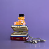 Hand opening ceramic graduation bear trinket box and lifting a silver keychain — detailed view of interior.