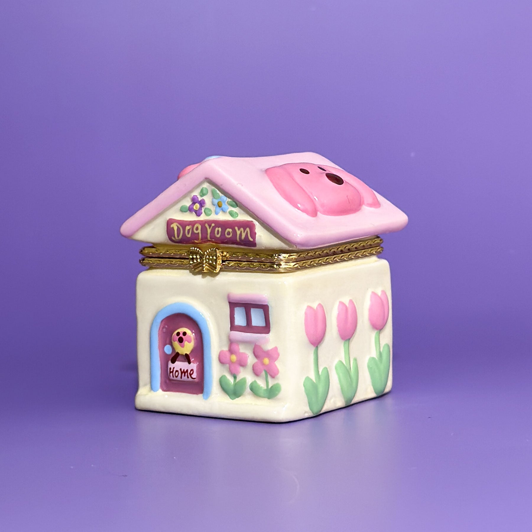 Side view of dog house trinket box with pink roof, tulip decorations, and gold hinge on purple background.